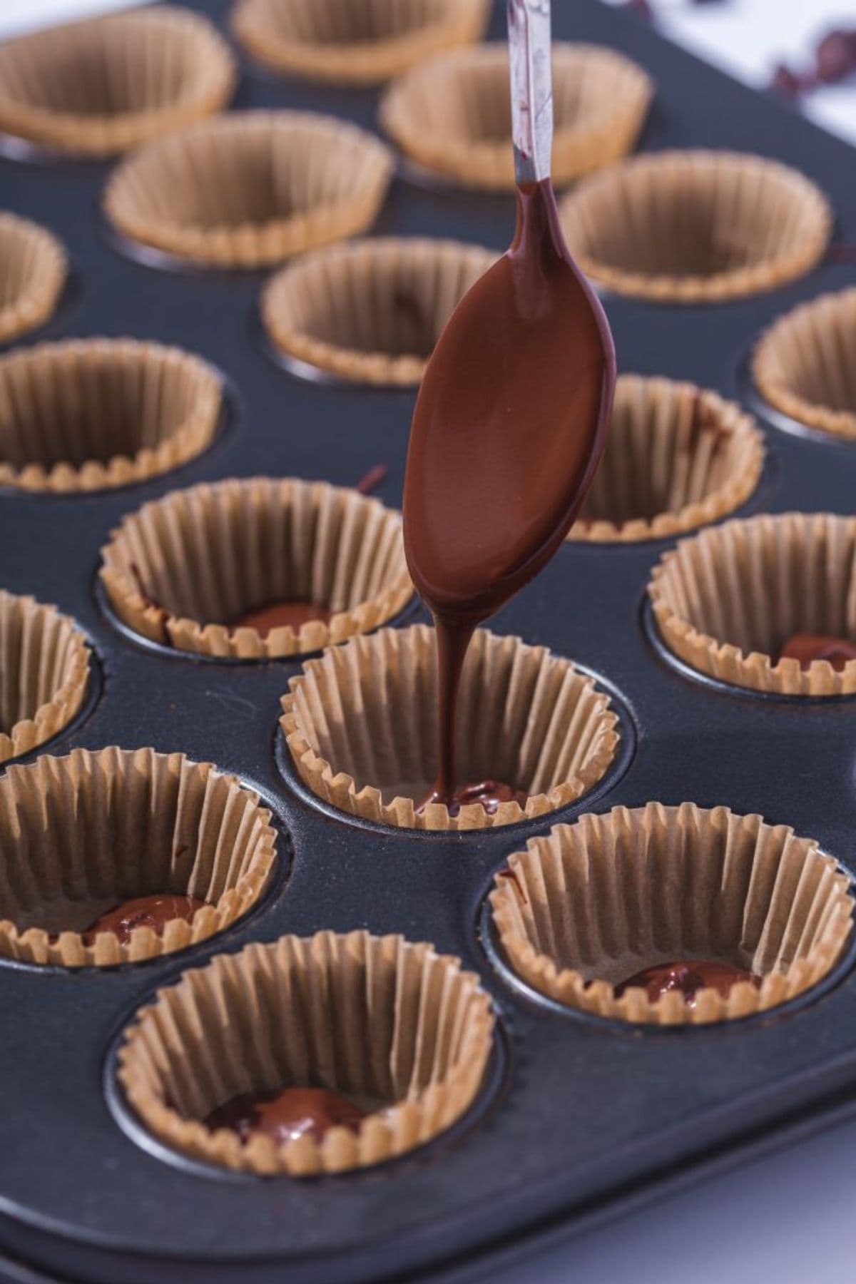 A spoon pouring melted chocolate into a tin lined with parchment paper.