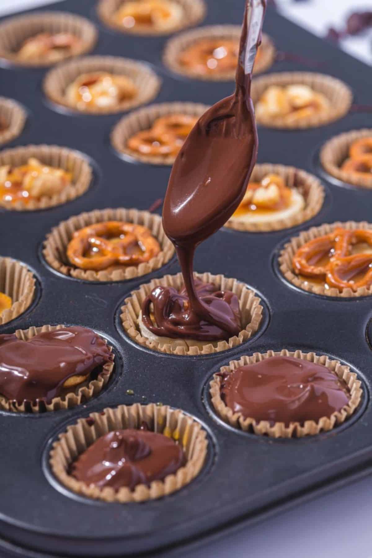 A spoon pouring melted chocolate into a parchment-lined tin, covering a banana slice filling inside.