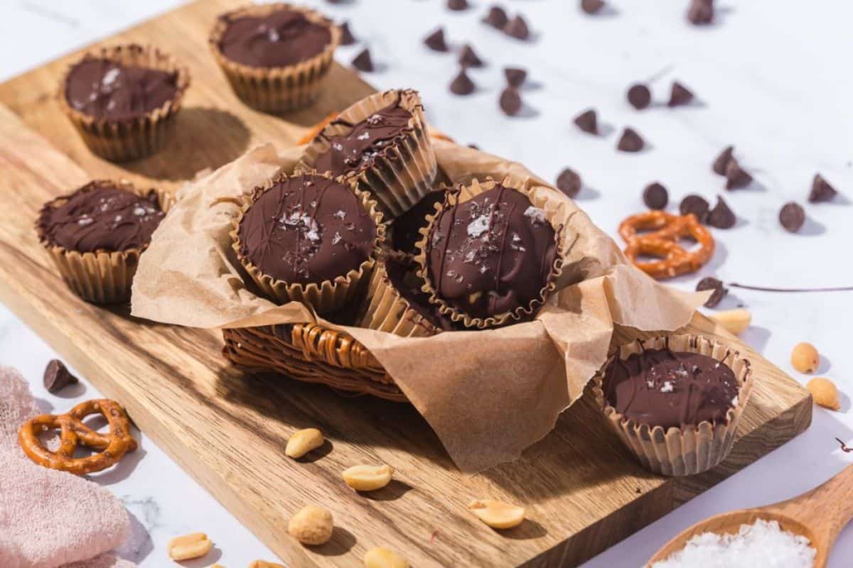 A stack of frozen banana bites with chocolate coating, pretzels, and peanuts served on a wooden board.