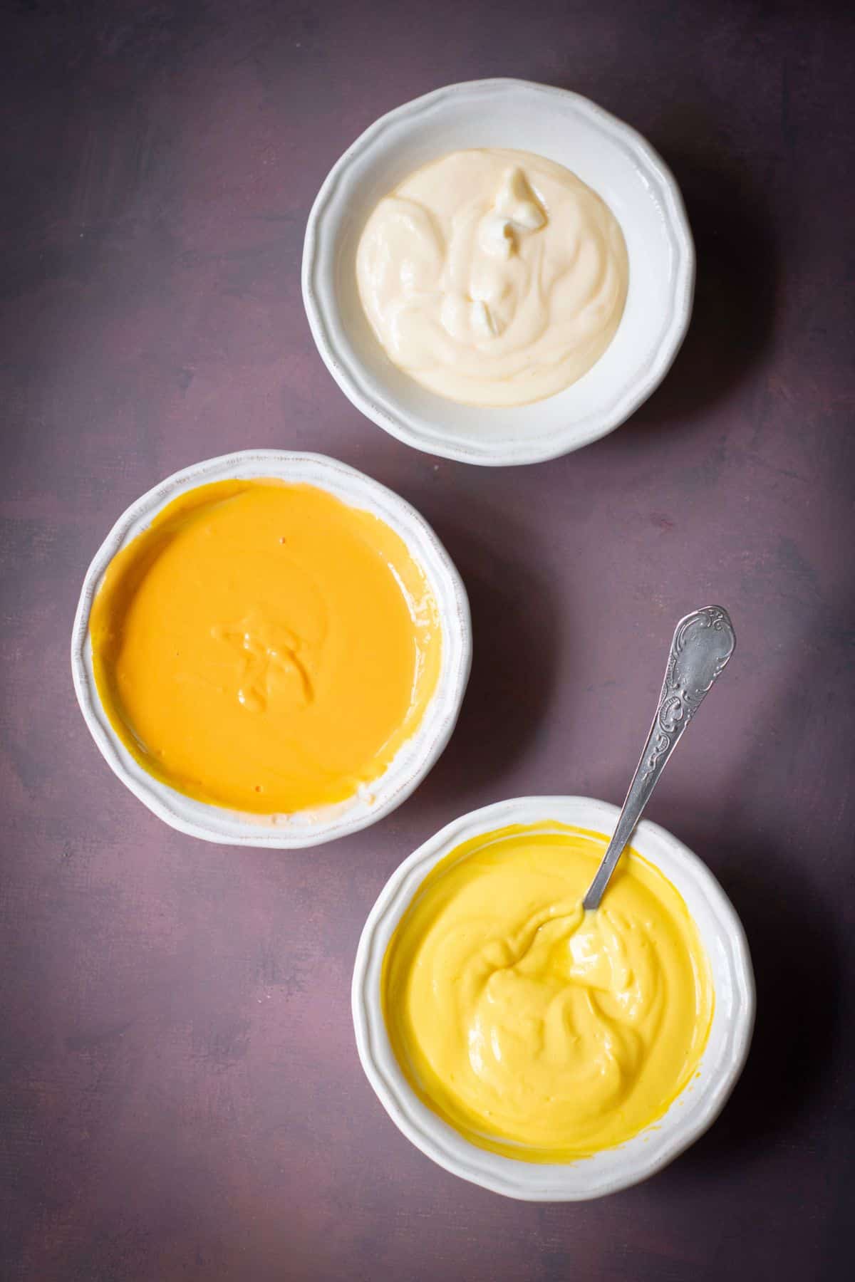 Three bowls of cheesecake batter in white, orange, and yellow, ready to be layered into tins.