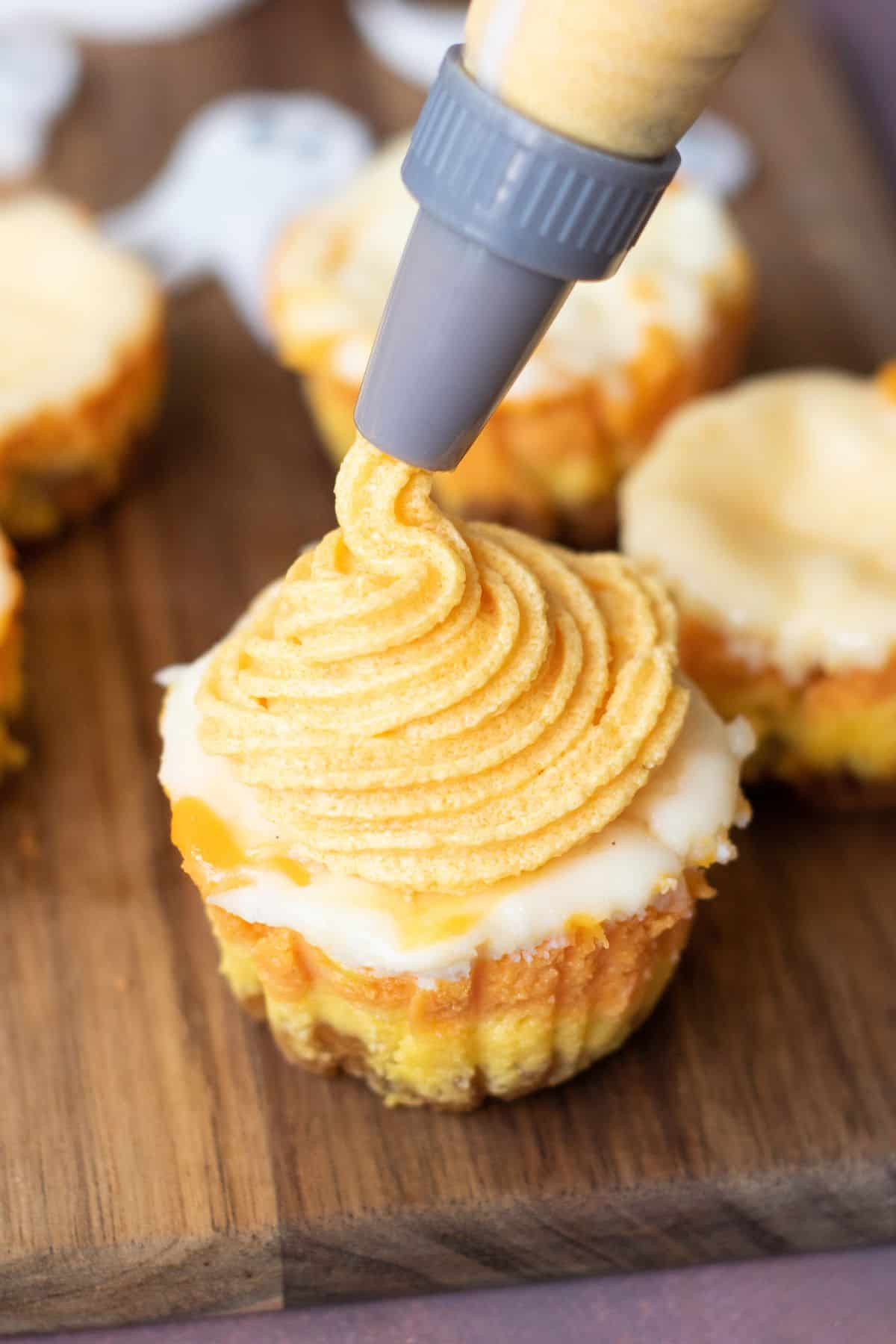 A single muffin being topped with yellow cheesecake batter from a piping bag.