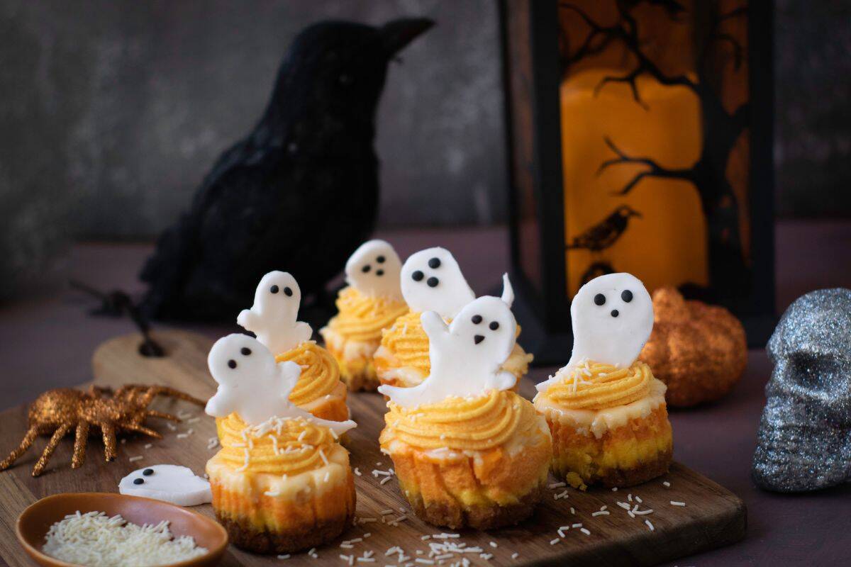 Mini Halloween cheesecakes with orange frosting and ghost toppers served on a wooden board.