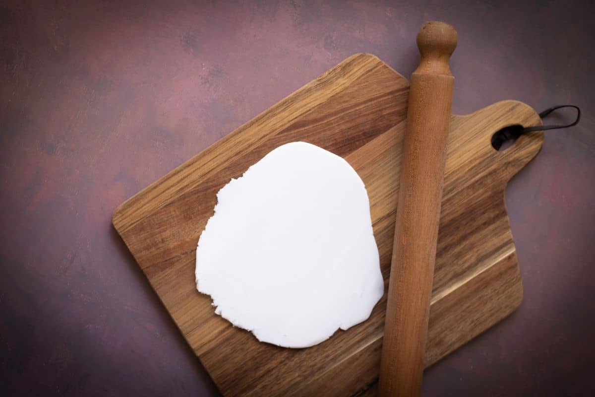 A mini candy corn cheesecake being flatten on a wooden board with a rolling pin beside it.