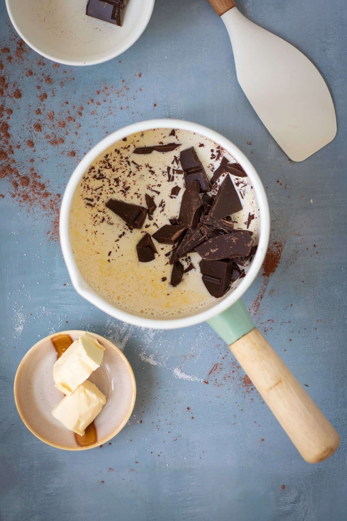 A chopped dark chocolate melting into warm heavy cream in a medium saucepan.