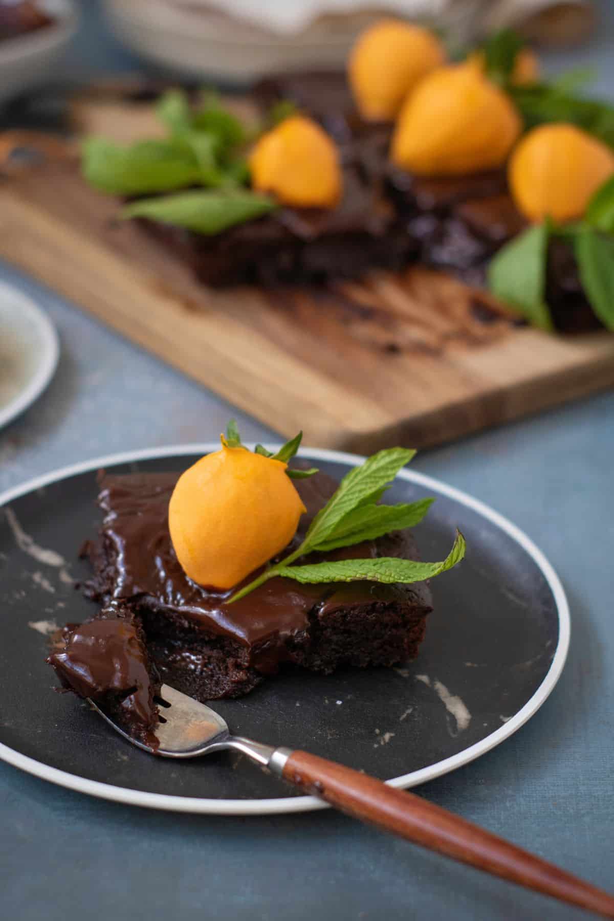 A single slice of chocolate pumpkin patch brownie cake on a white plate, topped with a candy-dipped strawberry and mint leaf garnish.