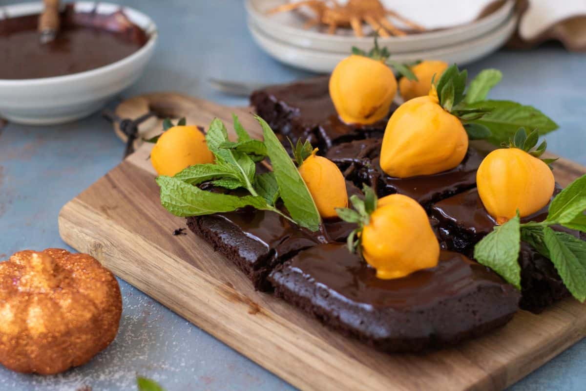 Chocolate pumpkin patch brownie cake being garnished with candy-coated strawberries and mint leaves, served on a rustic wooden board.