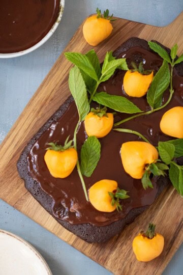 Chocolate pumpkin patch brownie cake being garnished with candy-coated strawberries and mint leaves, served on a rustic wooden board.