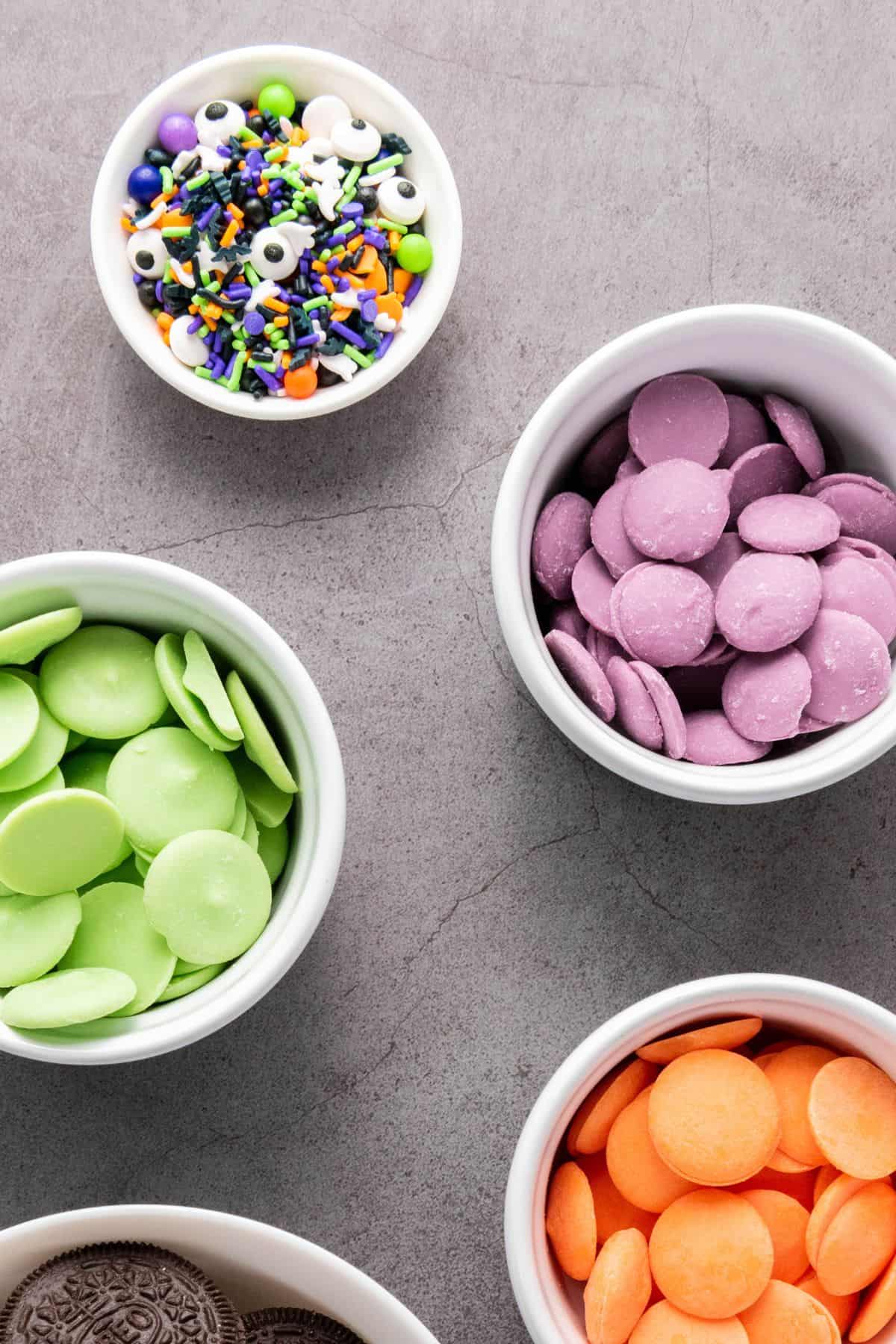 Small bowls filled with colorful Halloween candy melts and assorted festive sprinkles.
