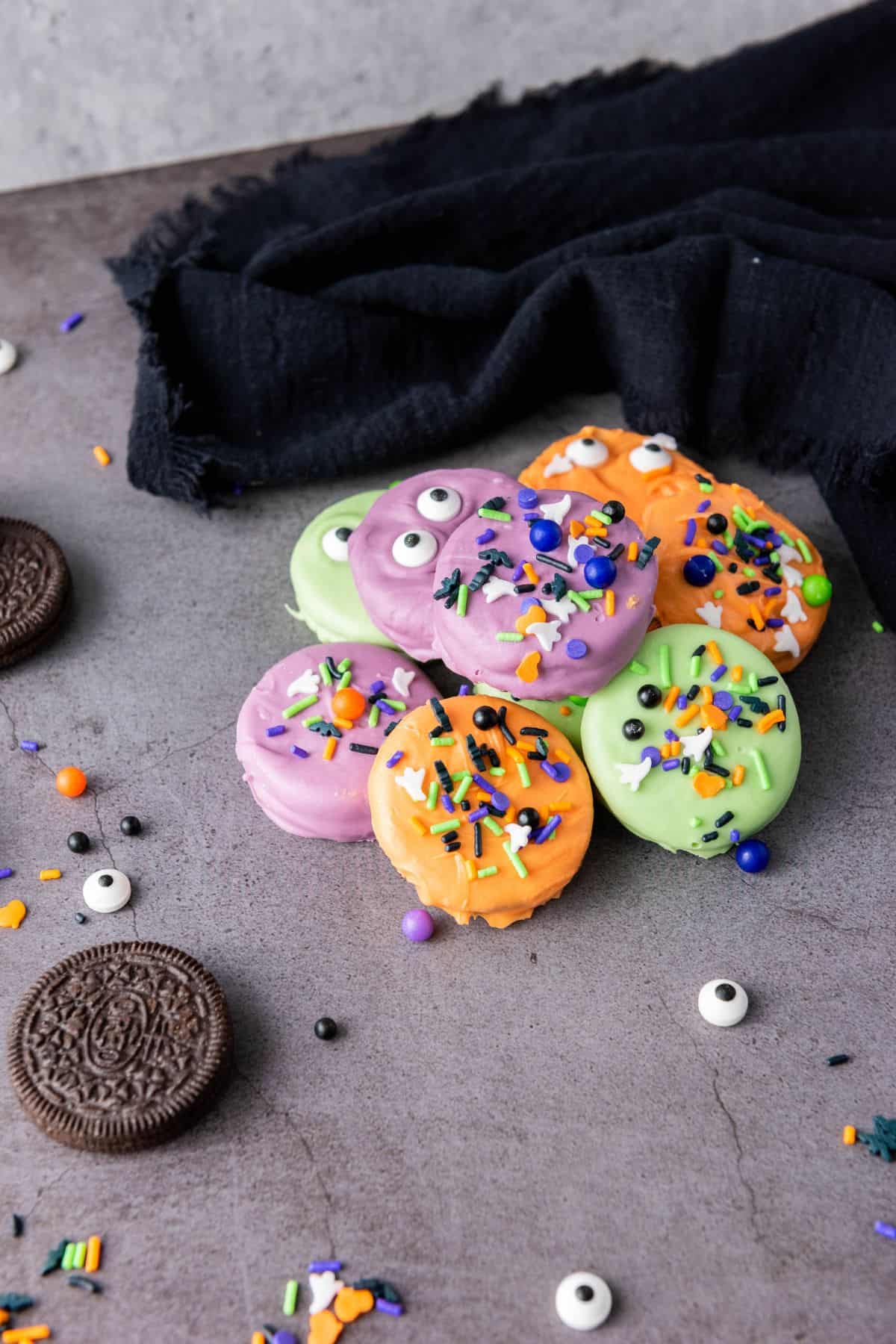 A plate full of colorful Halloween-dipped cookies surrounded by extra plain Oreos, ready to serve.
