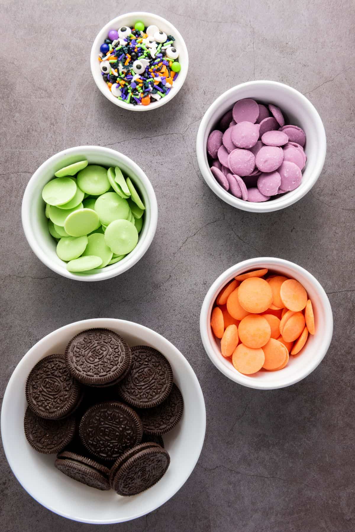 Halloween cookie ingredients neatly arranged on a flat surface, including Oreos, colorful candy melts, and festive sprinkles.
