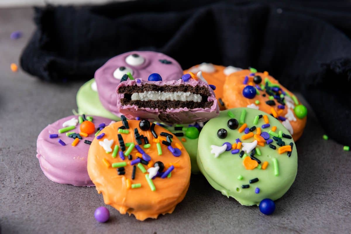 Stack of colorful Halloween cookies with one cookie showing a bite taken out, revealing the Oreo inside.