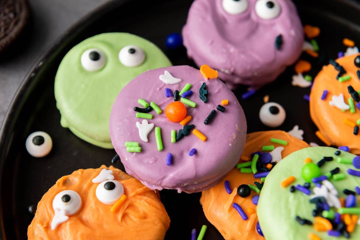 Close-up of a plate full of Halloween-themed cookies coated in purple, green, and orange candy, topped with festive sprinkles.