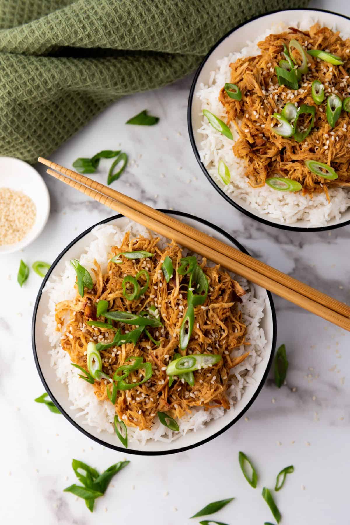 Chicken in soy honey garlic sauce served in a bowl with rice and chopsticks beside it.