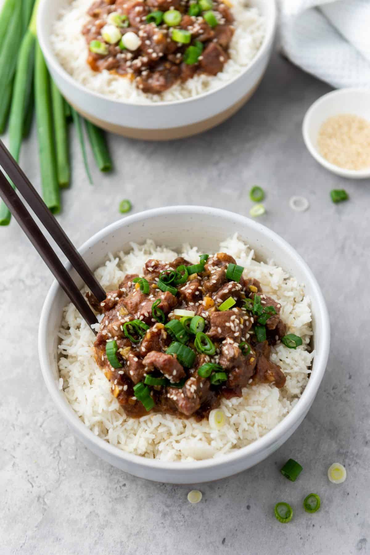 Mongolian beef served in a bowl with rice, chopsticks resting on top.
