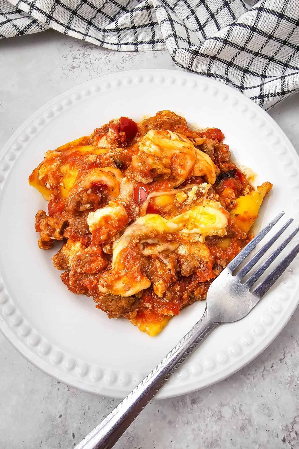 A slice of lasagna served on a plate with a fork beside it.