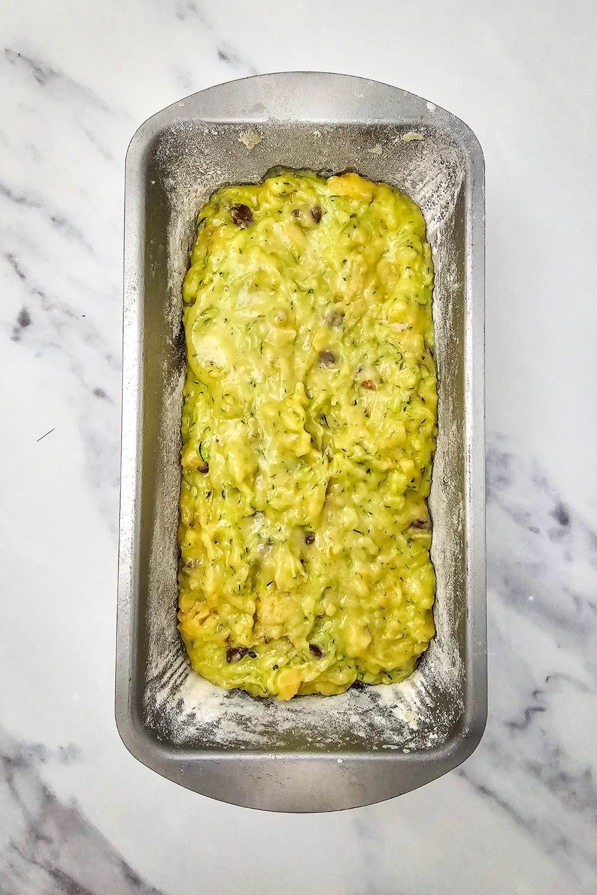 Batter being poured and spread into a loaf pan for baking.