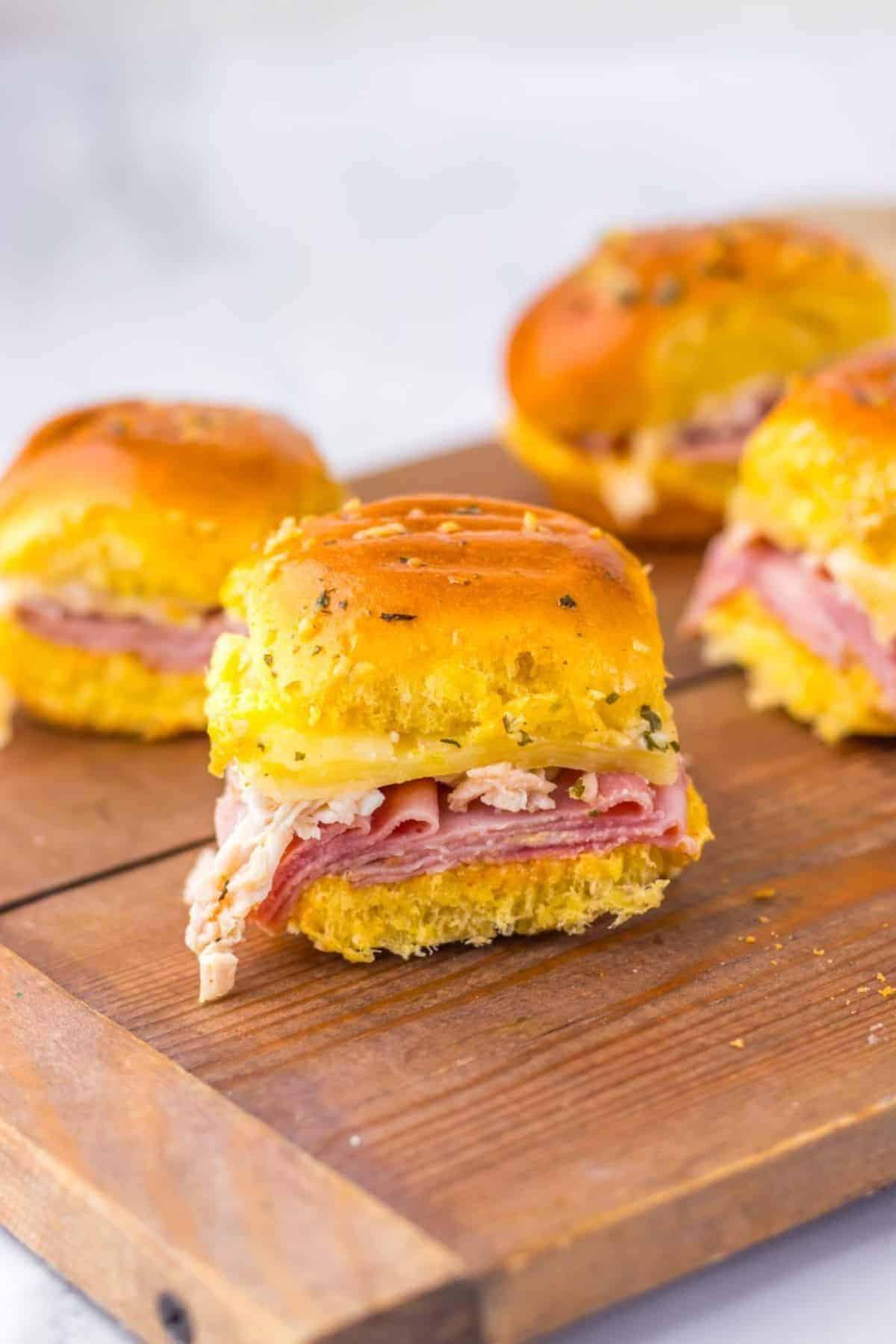Chicken cordon bleu sliders on hawaiian rolls served on a wooden board.