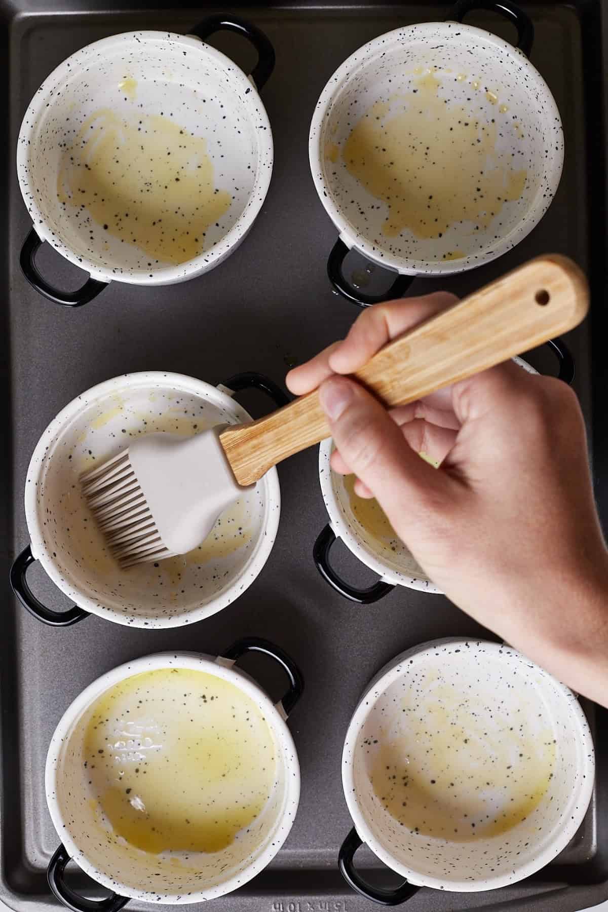 A hand brushing each ramekins with melted butter.