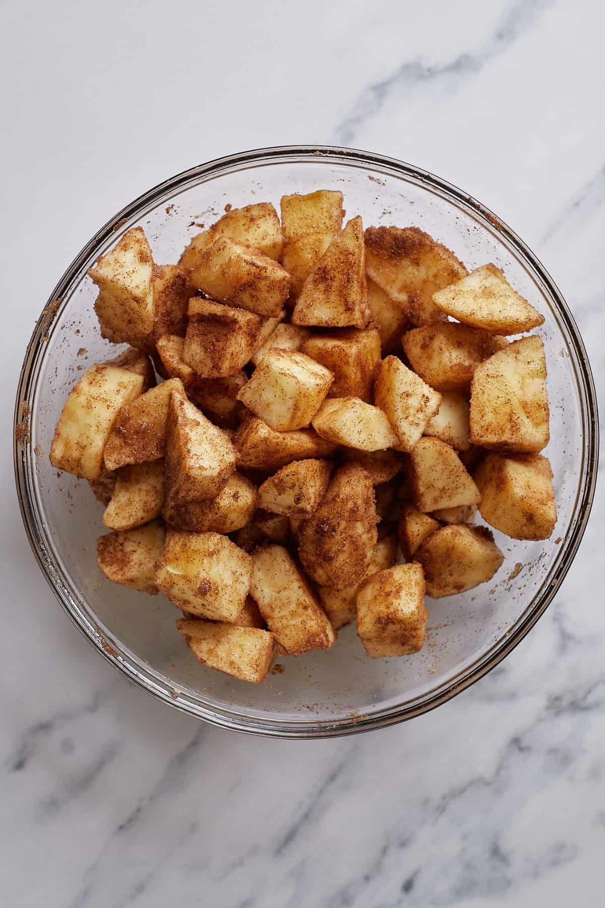 Sliced apples in a bowl, seasoned with brown sugar, cinnamon, and nutmeg.