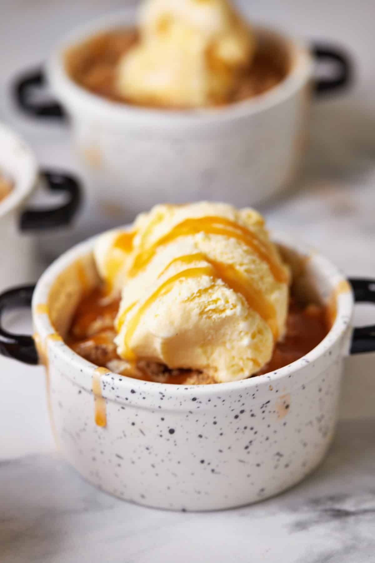 Close-up of a mini apple crumble in a small bowl, topped with golden oat crumble and a scoop of melting vanilla ice cream.