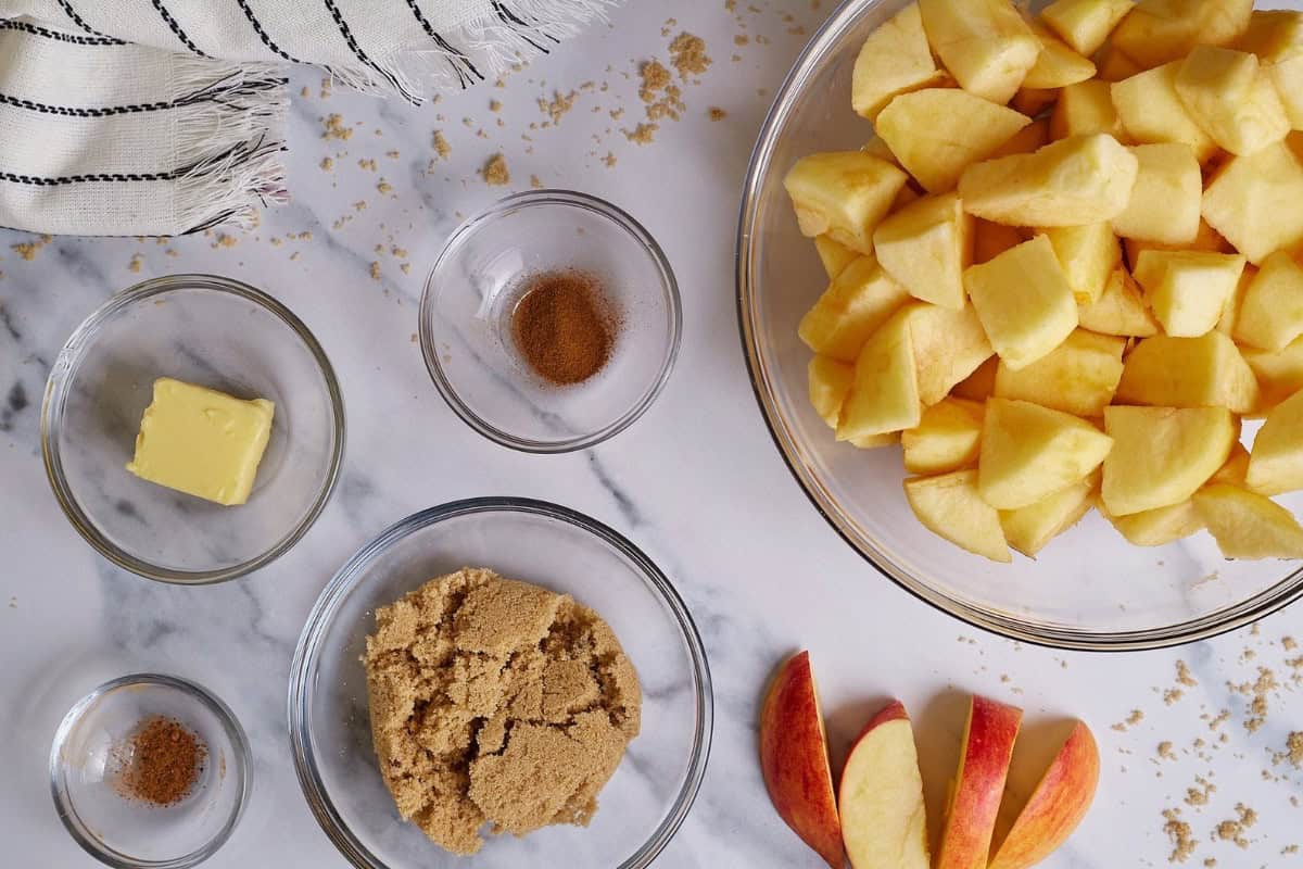 Flat lay of apple crumble ingredients arranged neatly on a surface, including apples, oats, flour, butter, sugar, and spices.