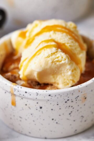 Close-up of a mini apple crumble in a small bowl, topped with golden oat crumble and a scoop of melting vanilla ice cream.