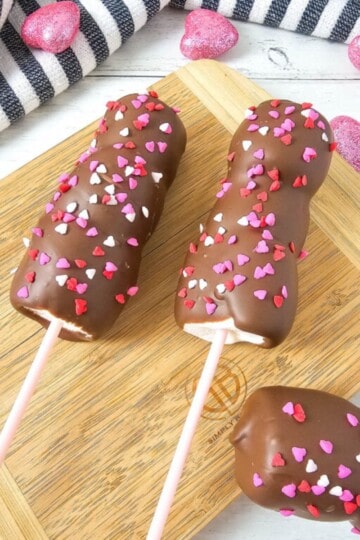 Chocolate-covered marshmallow pops served on a wooden board, decorated with heart sprinkles.