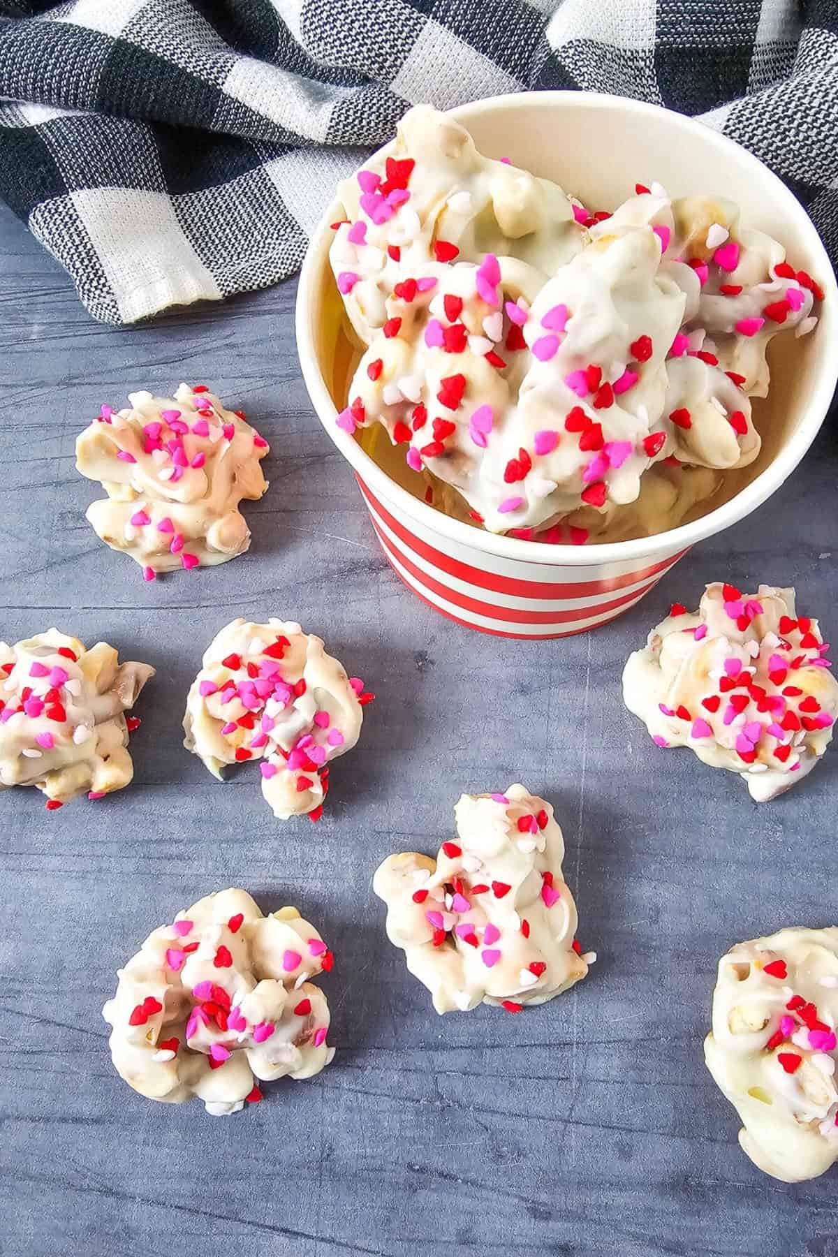 White chocolate candies on a surface next to a bucket of more candies.