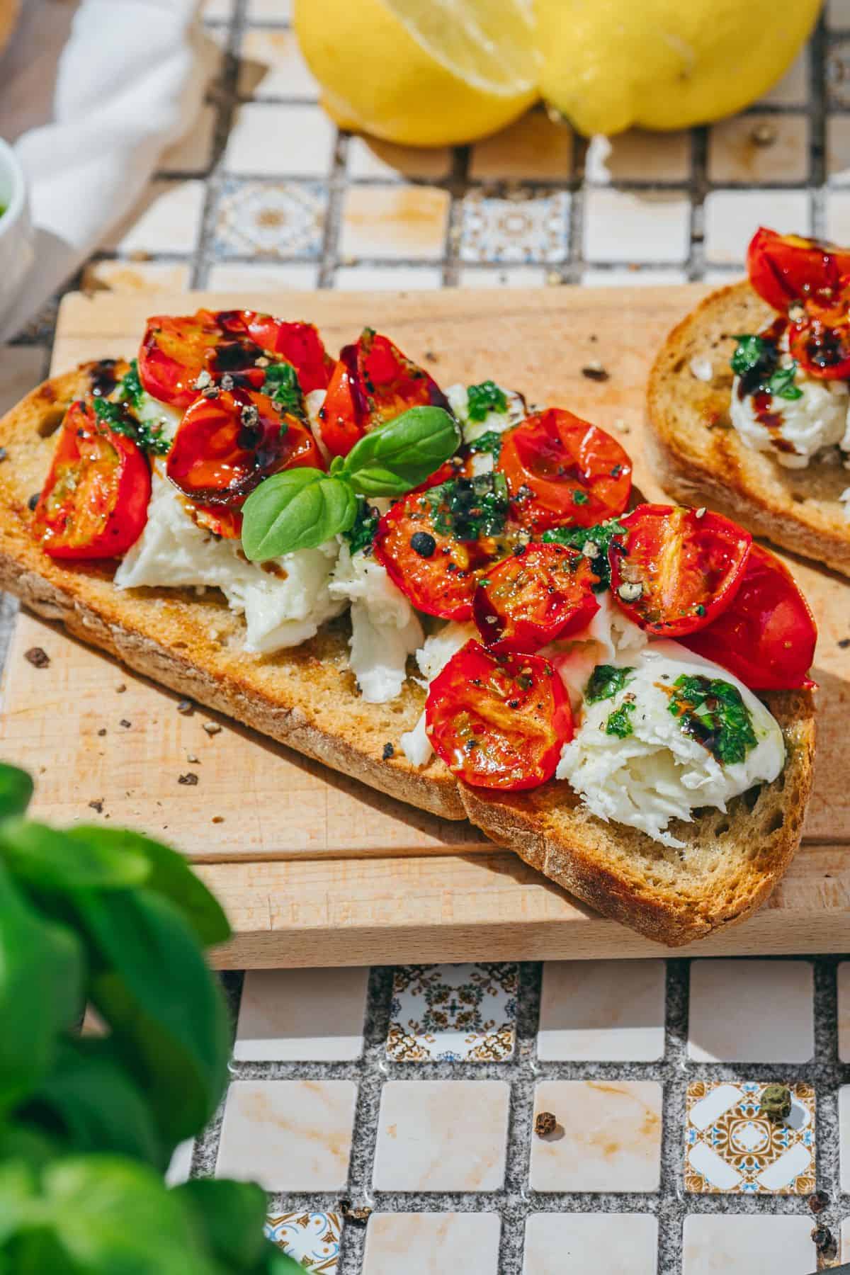 Close-up of savory burrata toast topped with roasted tomatoes and basil drizzle, served on a cooling tray.