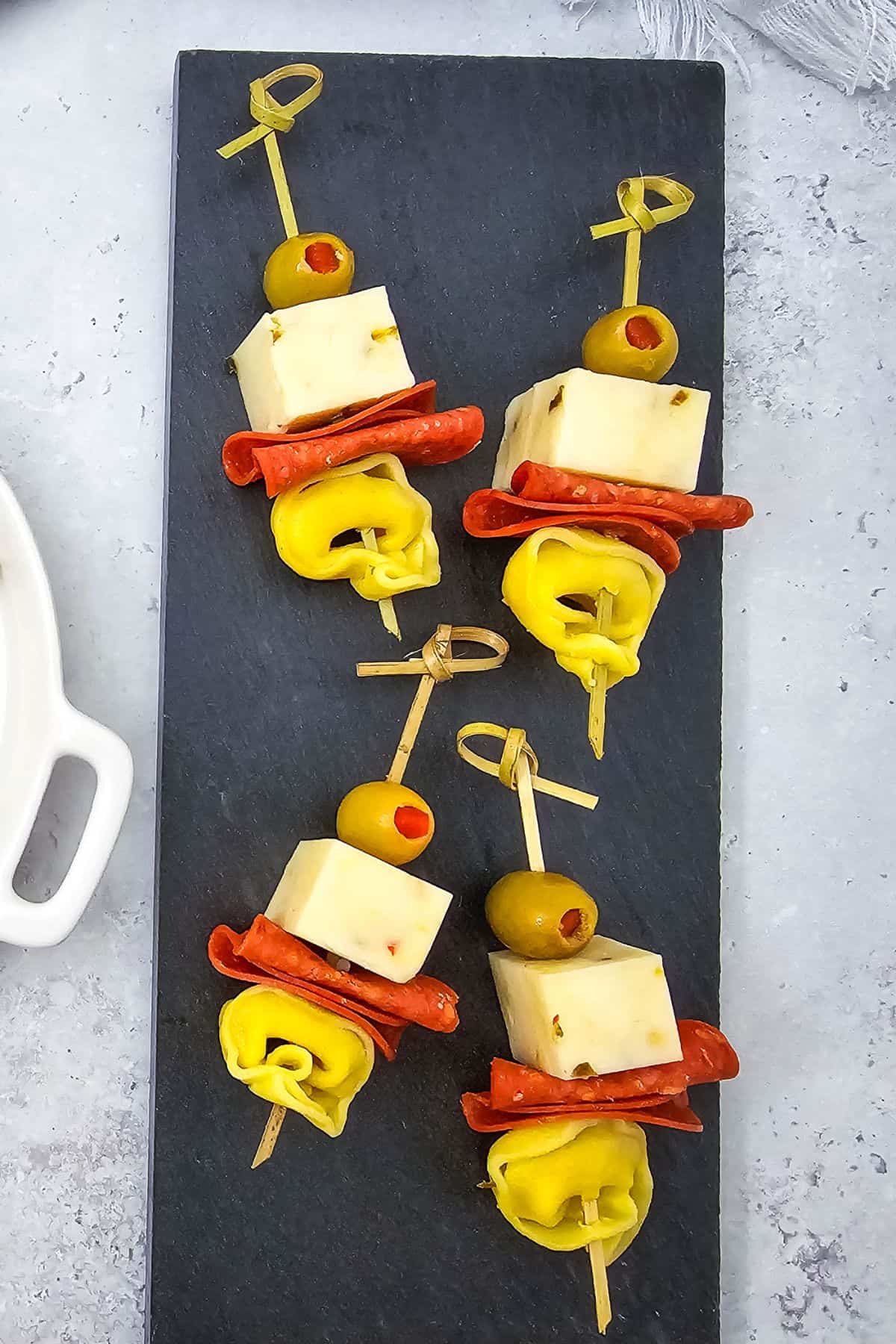 Tortellini skewers with pepperoni and olives being served on a plate.