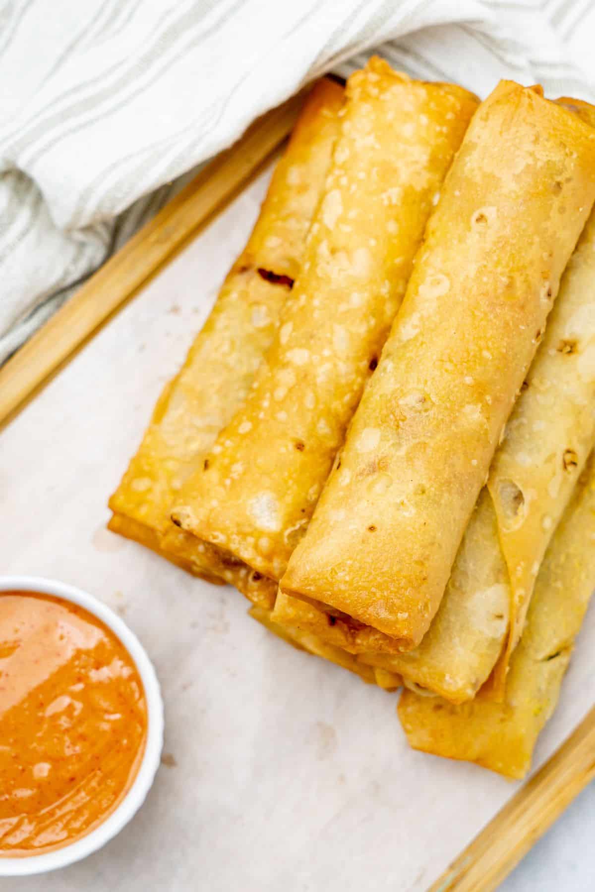 Close-up of crispy chicken and vegetable spring rolls with a small bowl of dipping sauce on the side.