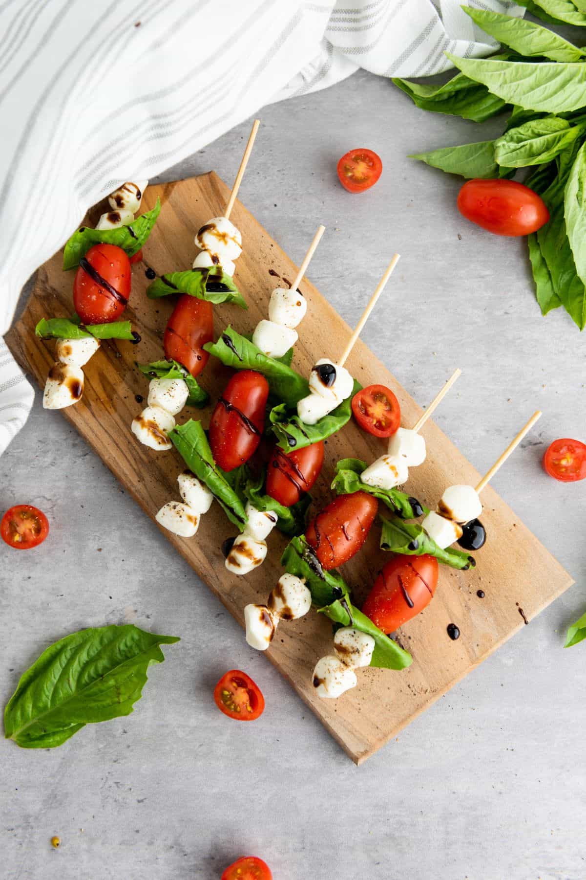 Skewers with cherry tomatoes, mozzarella, and basil neatly arranged on a wooden board.