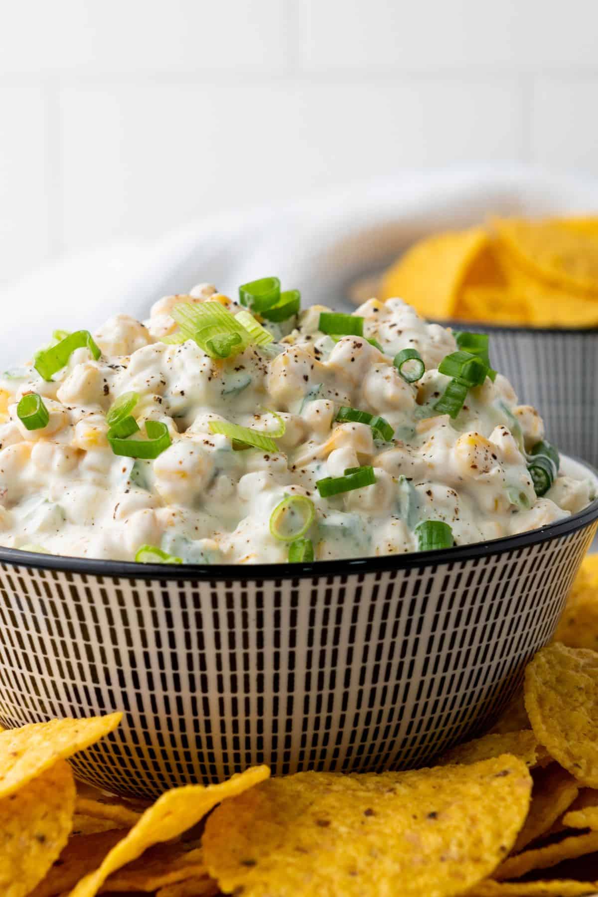 A bowl of corn dip surrounded by tortilla chips.