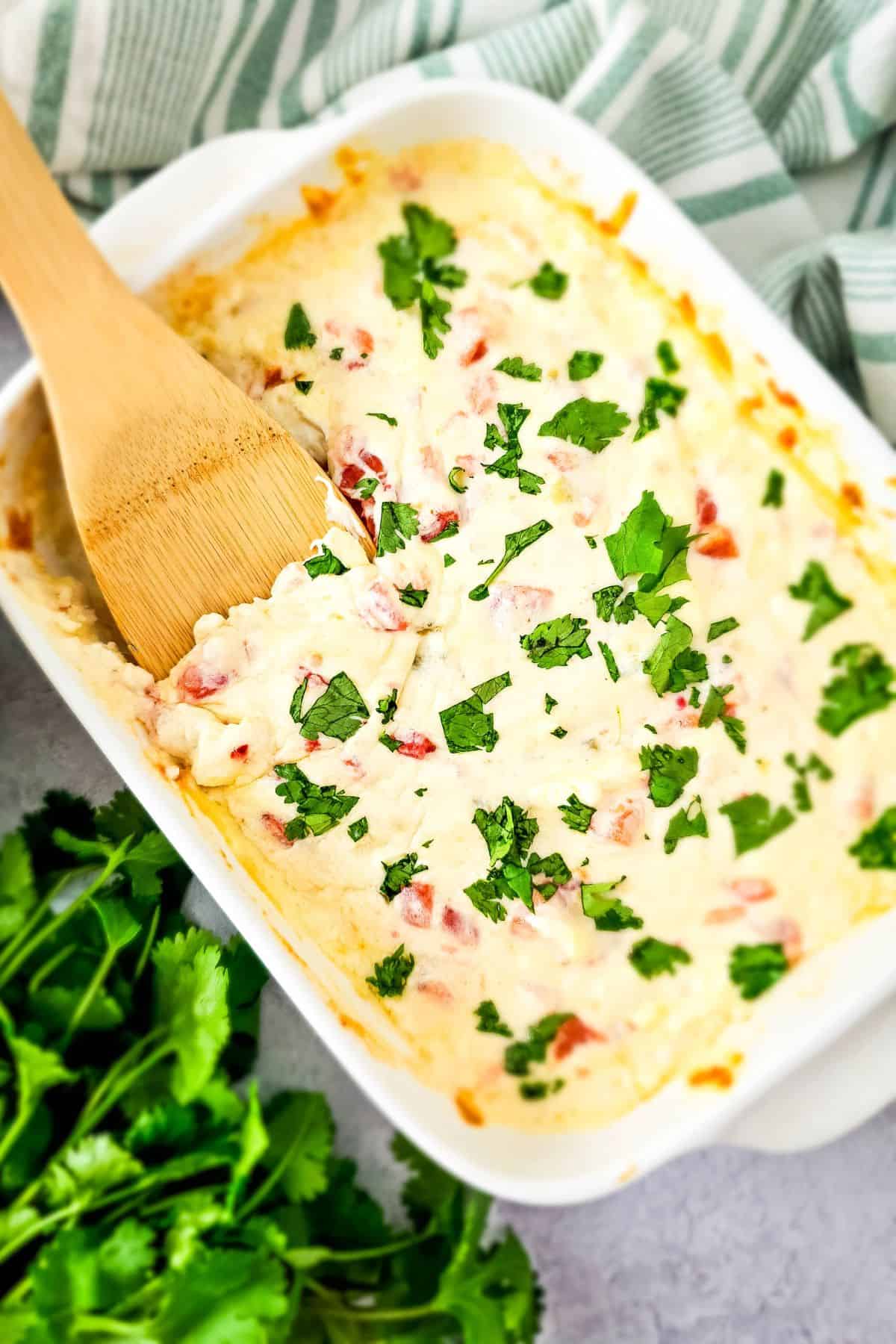 Simple loaded queso dip being scooped from a serving dish with a spatula.