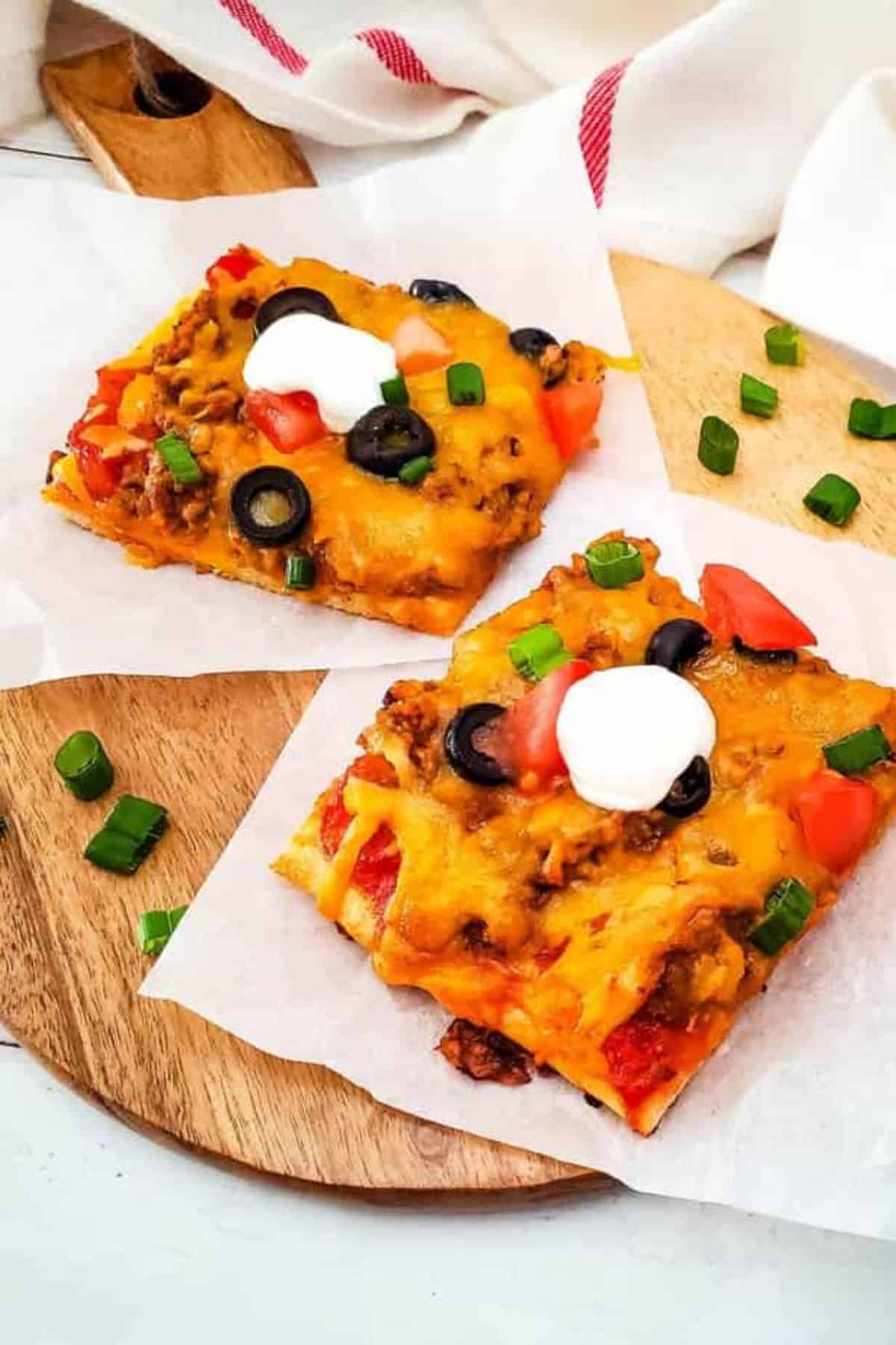 Two slices of taco pizza served on a plate with a paper towel in the background.
