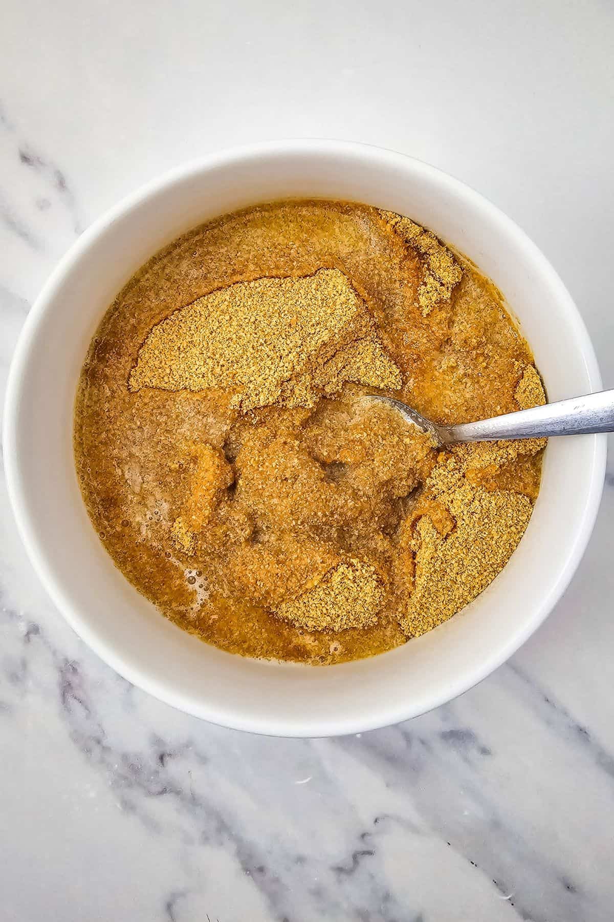 Graham cracker crumbs being mixed with melted butter in a bowl using a spoon.