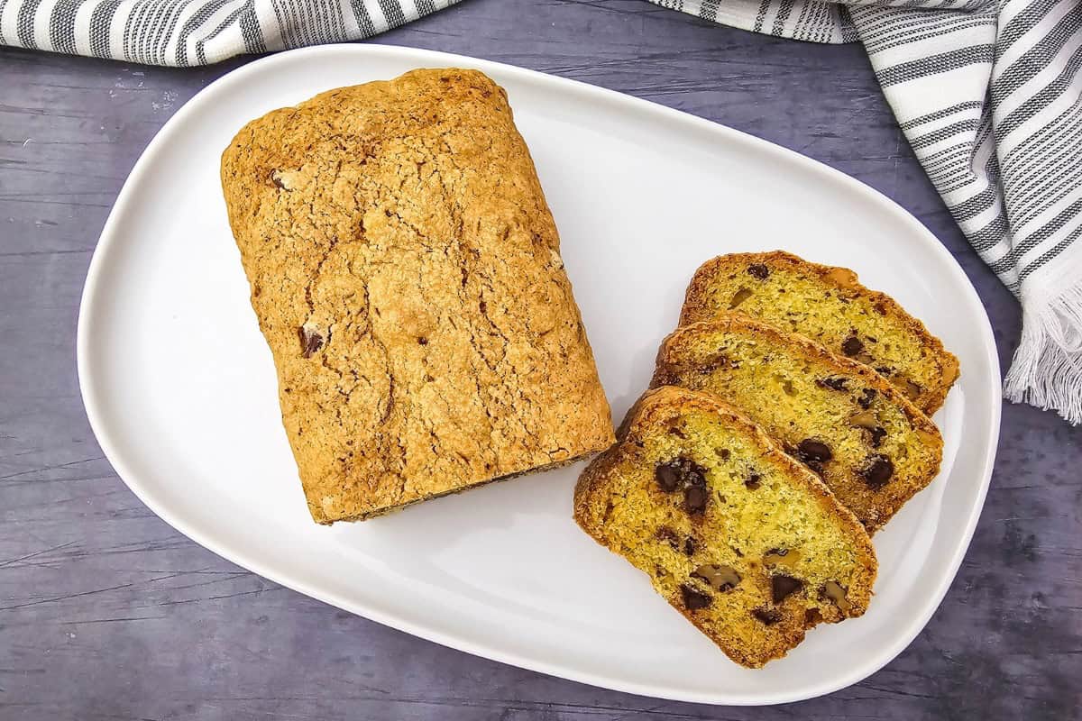 A loaf of bread with three slices on a plate beside it.