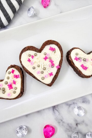 Three fudgy brownie hearts with white chocolate frosting served on a plate.