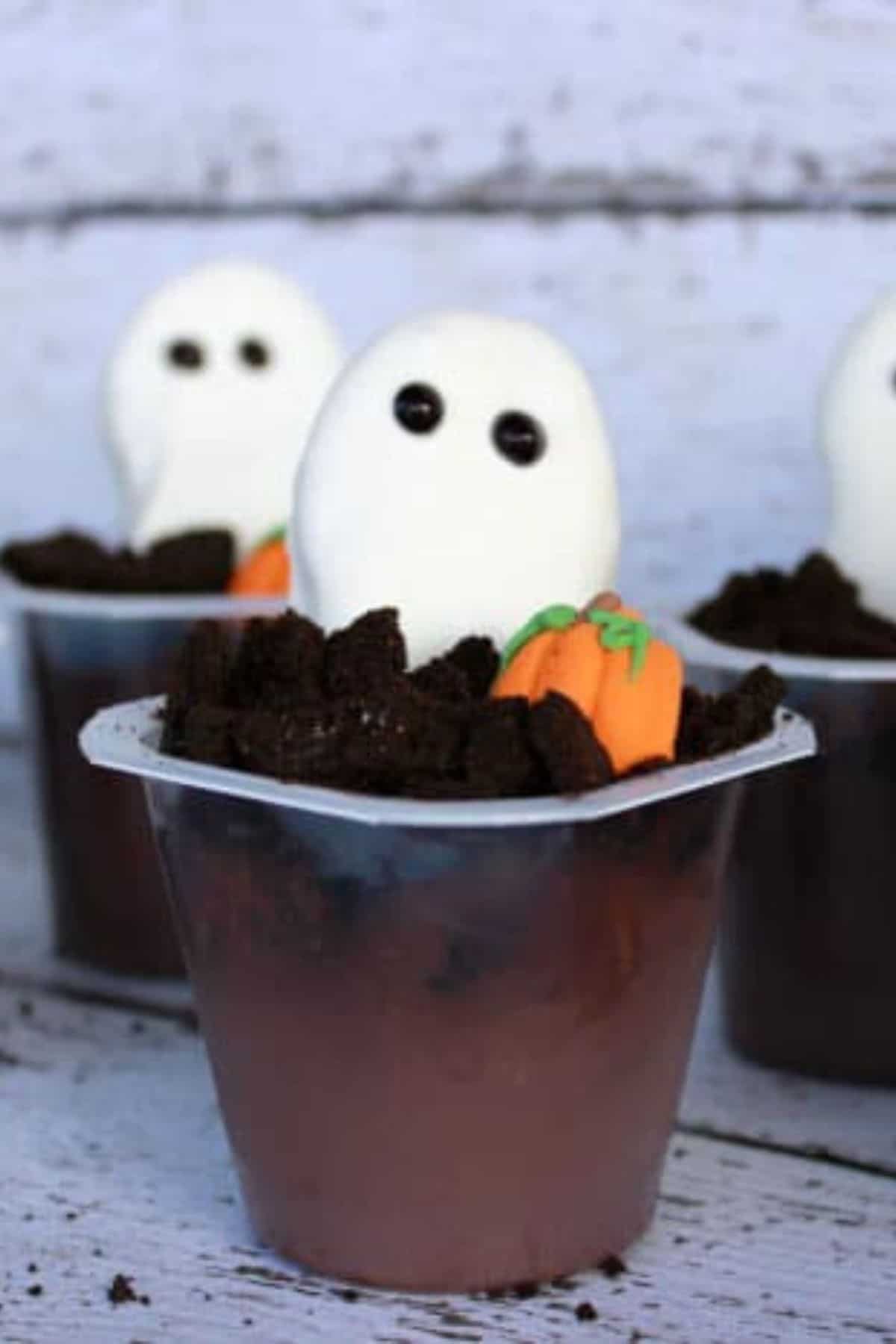 Close-up of decorated Halloween pudding cup with whipped topping and candy eyes, with additional pudding cups blurred in the background.