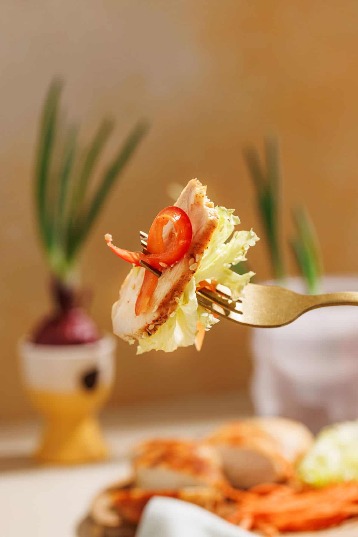 A fork lifting a portion of Asian sesame chicken salad from a white plate, showcasing the colorful mix of vegetables and chicken.