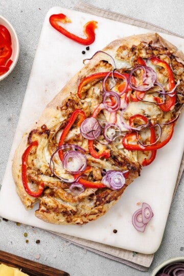 A flatbread being sliced, served with tomato and onion on the side.