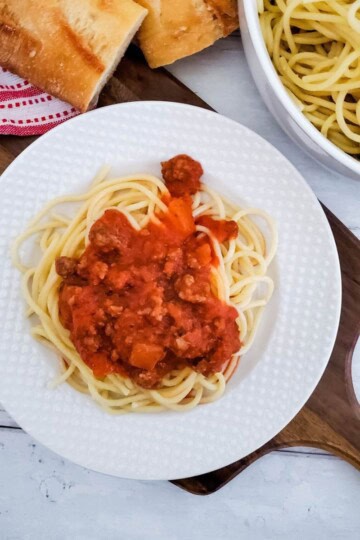 Plate of spaghetti topped with beefy meat sauce, served with extra sauce on the side.