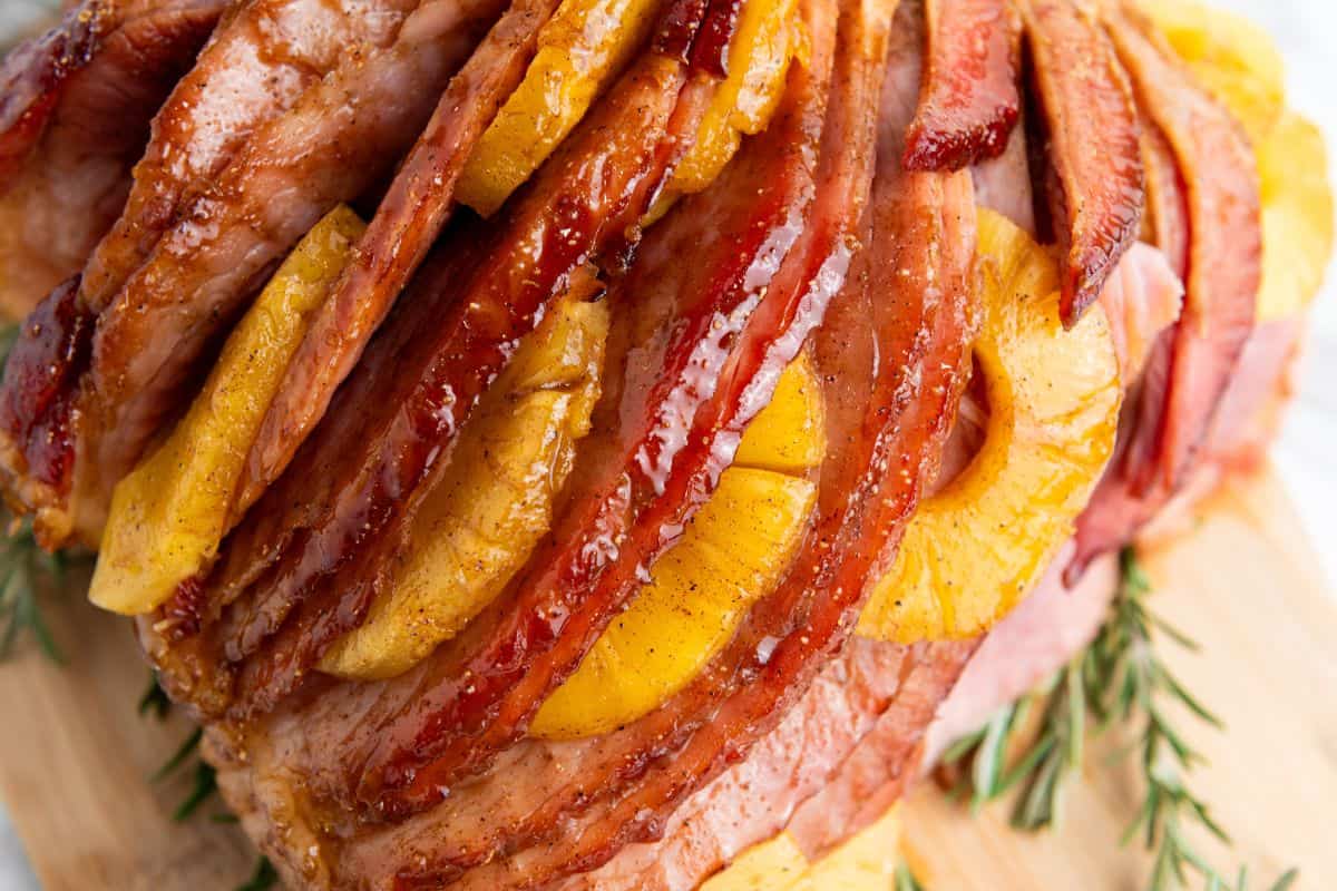 Close-up photo of a serving of brown sugar pineapple ham sliced and arranged, garnished with pineapple rings, a light glaze, and sprigs of rosemary around the edges.