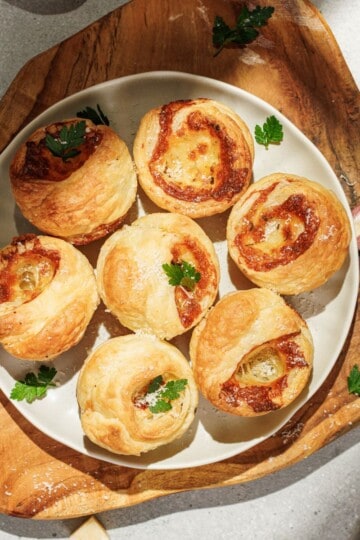 Freshly baked cheesy garlic cruffins served on a plate under a wooden board, garnished with chopped parsley.