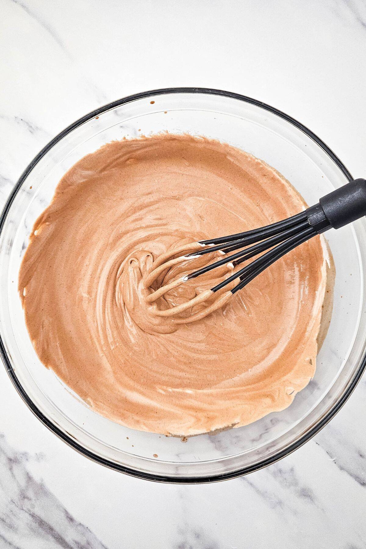 A large bowl filled with chocolate mixture, with a whisk resting on top.