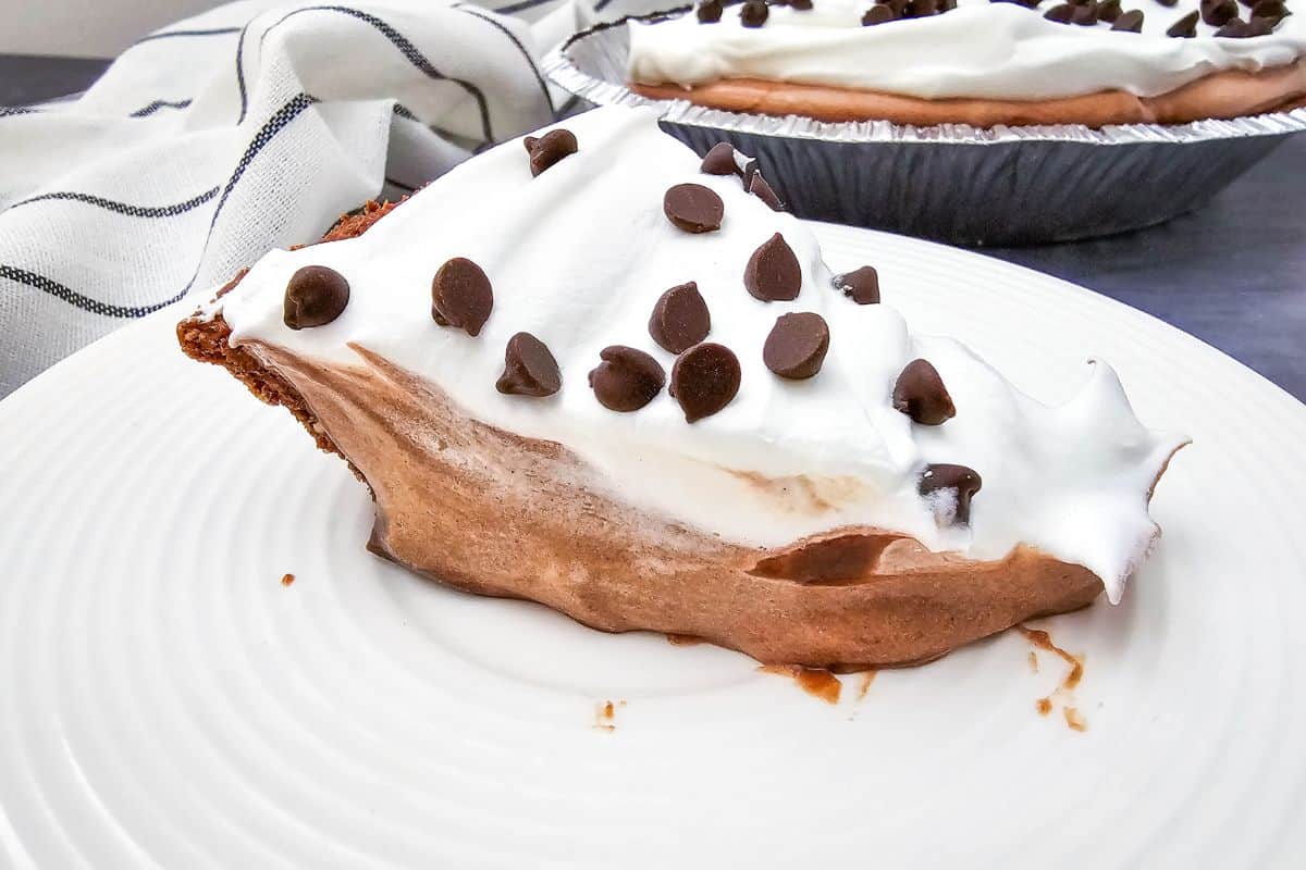 Close-up photo of a slice of chocolate pie with whipped cream and chocolate chips on a plate.