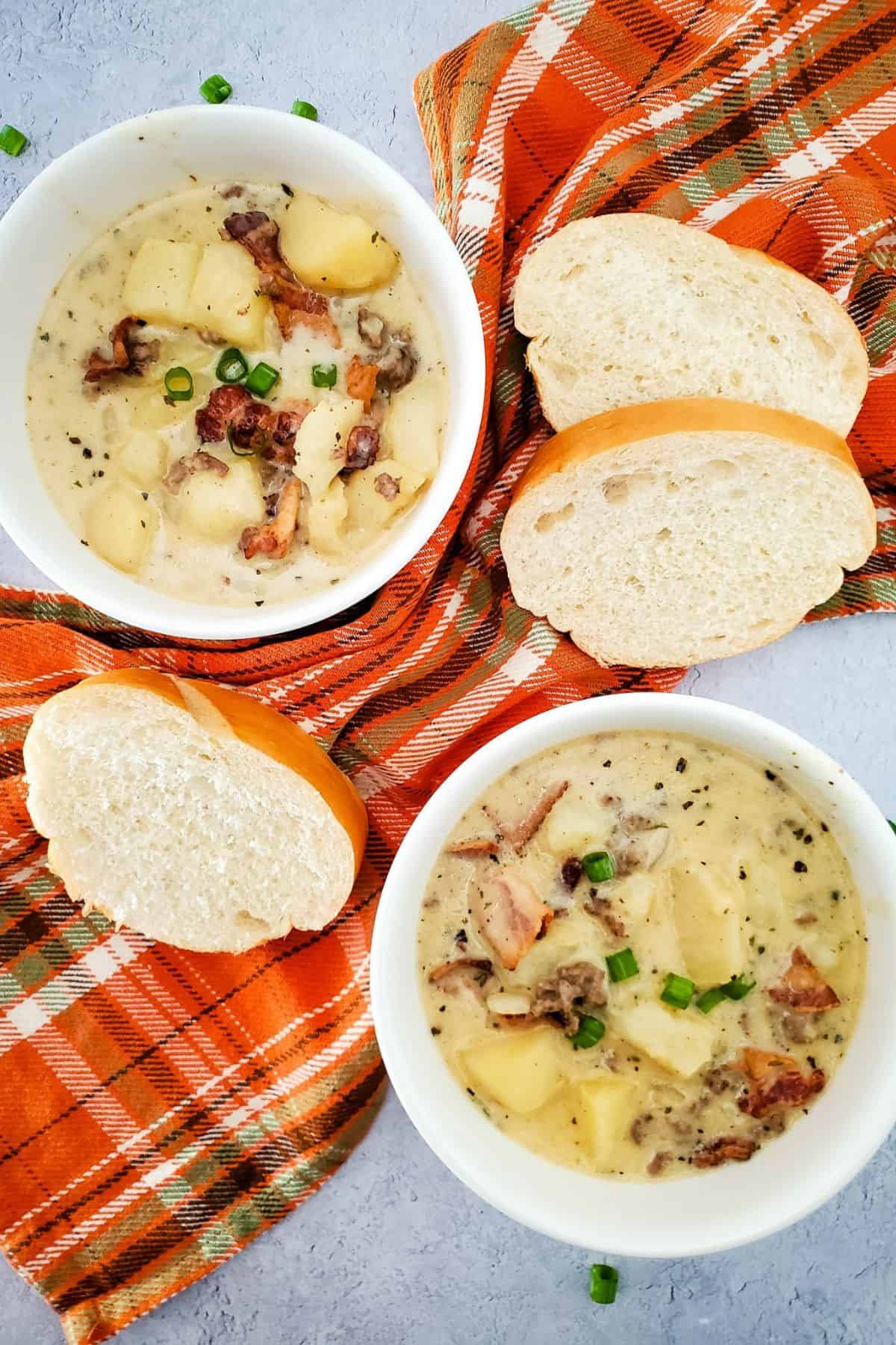 Two bowls of creamy cheeseburger potato soup served with slices of crusty bread on the side.