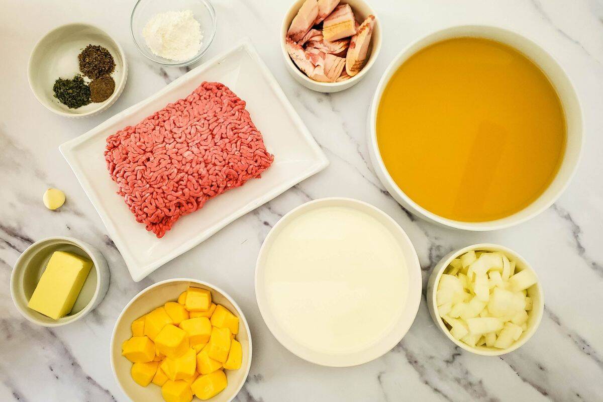 Neatly arranged soup ingredients on a kitchen surface, including diced potatoes, ground beef, bacon, onion, garlic, and seasonings.