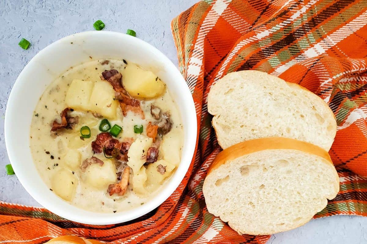 A single bowl of steaming soup with a slice of bread beside it, resting on a cloth-covered surface.