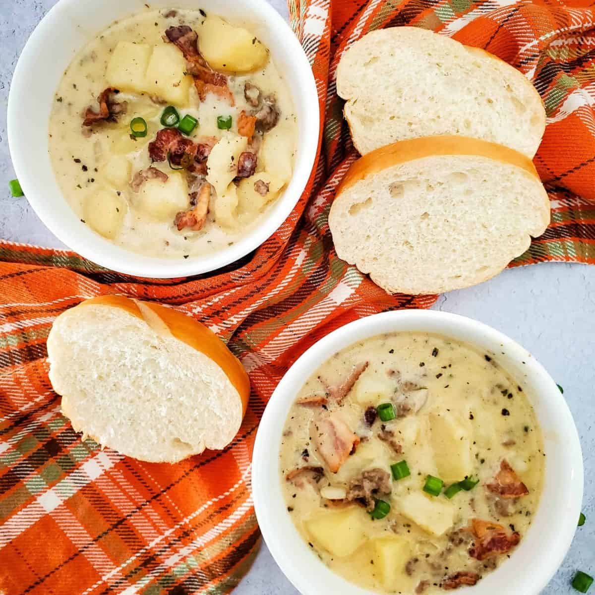 Two bowls of creamy cheeseburger potato soup served with slices of crusty bread on the side.